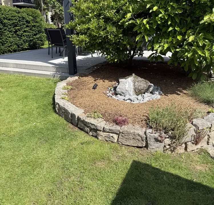 Natursteinbeet mit Solitärstein und Neubepflanzung neben der Terrasse