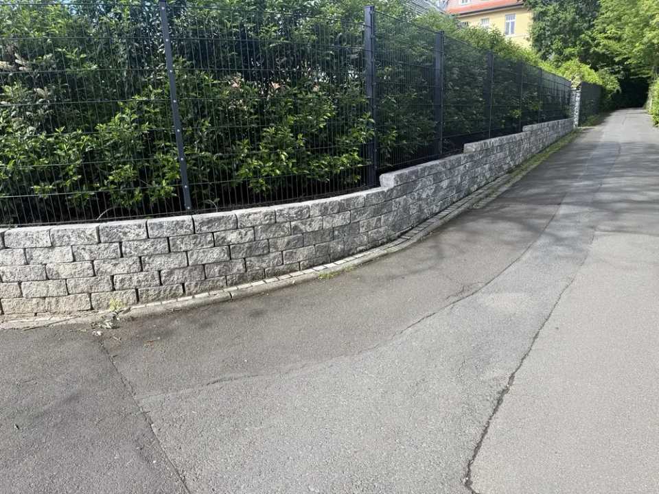 Fertige Natursteinmauer mit Zaunanlage und Heckenpflanzung entlang der Grundstücksgrenze