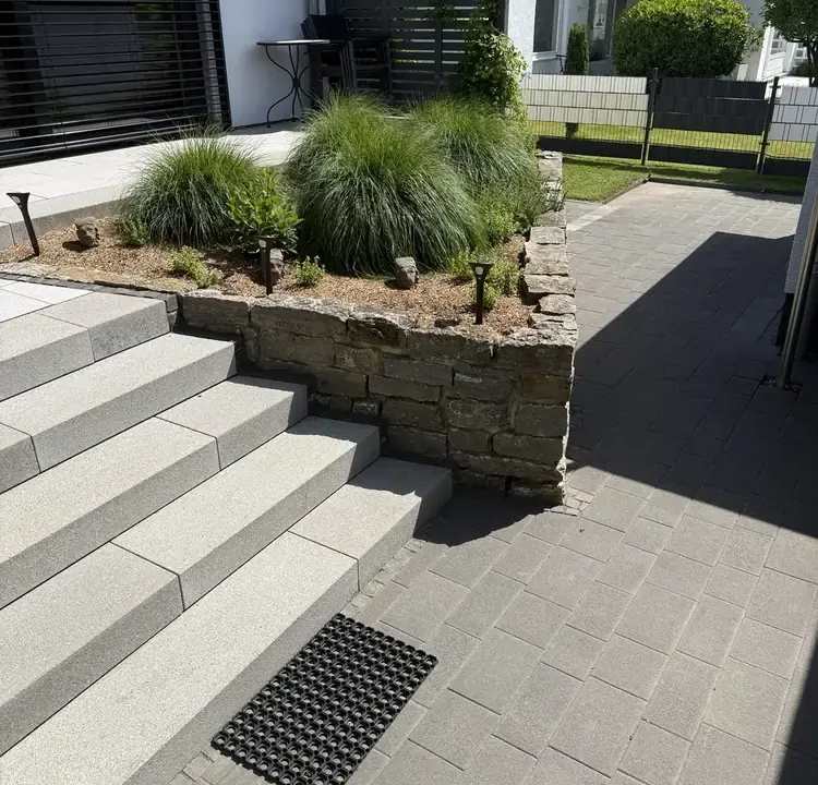 Treppenanlage aus hellen Betonstufen mit angrenzender Natursteinmauer und Pflasterfläche