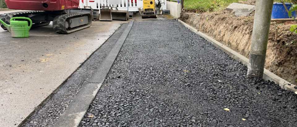 Abgesenkter Bordstein mit frisch eingebauter Asphalttragschicht im Gehweg- und Einfahrtsbereich