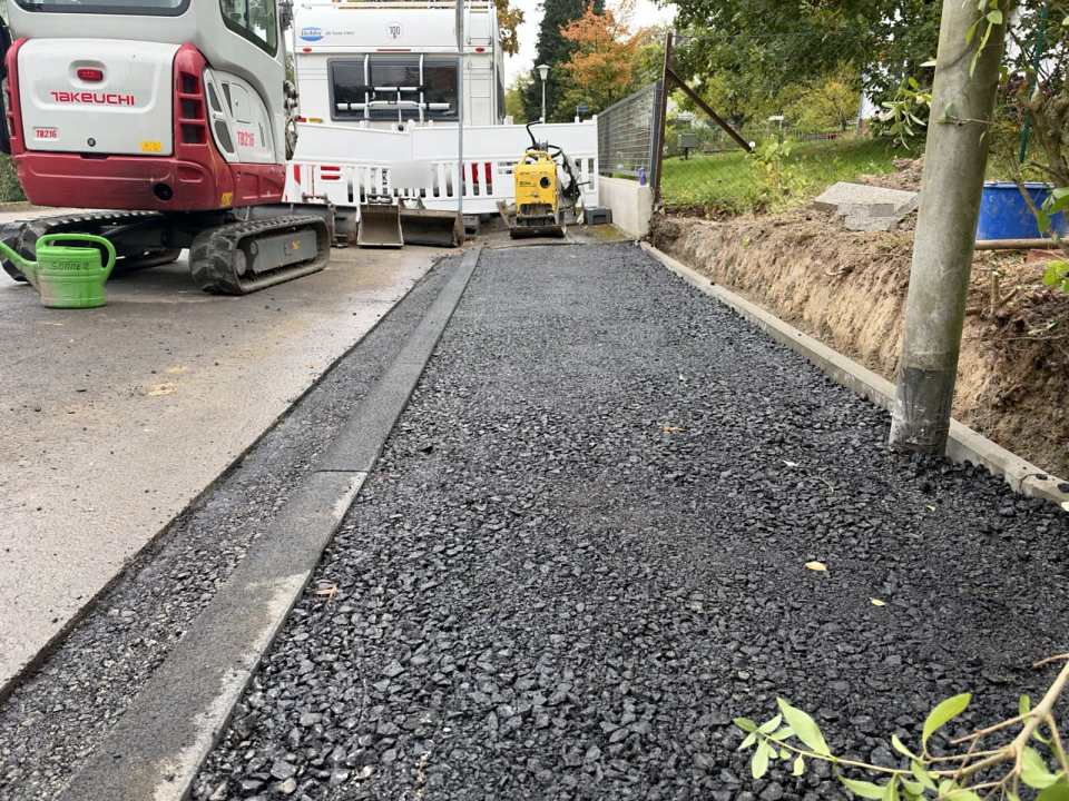 Abgesenkter Bordstein mit frisch eingebauter Asphalttragschicht im Gehweg- und Einfahrtsbereich