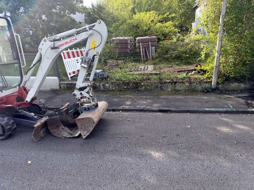 Ausgangslage vor der Bordsteinabsenkung in Kassel: Minibagger von Sommer Service am alten Gehweg mit Hochbord