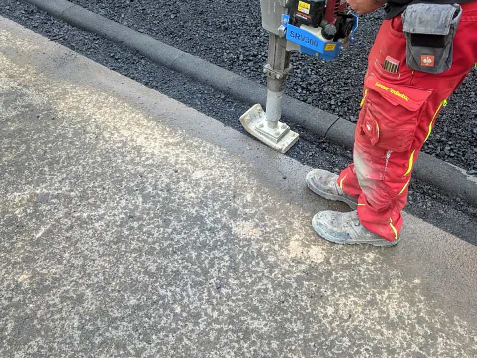 Verdichten des Asphaltanschlusses am Rundbordstein mit dem Vibrationsstampfer – Sommer Straßenbau