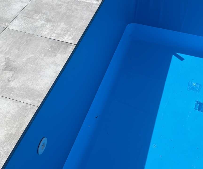 Verlegte großformatige Beckenrandplatten entlang des blauen Poolbeckens