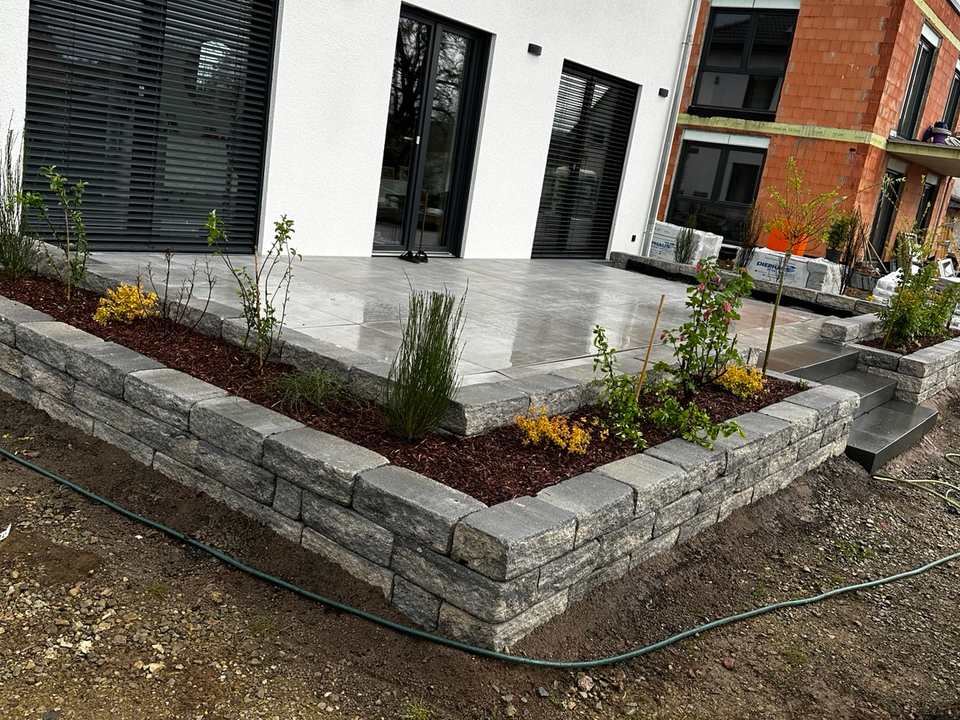 Moderne Außenanlage mit Terrasse, Natursteinmauer und Pflanzflächen
