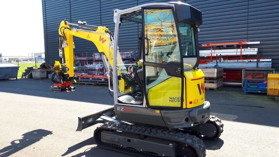 Gelber Kompaktbagger mit Raupenfahrwerk und hydraulischem Anbaugeräte-Wechsler auf einem Betriebsgelände
