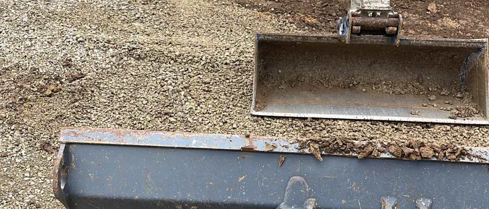 Baggerarm und Löffel bei Erdarbeiten in einer abgesperrten Baugrube mit Anschlusskasten am Straßenrand