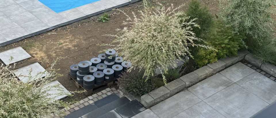 Blauer Pool mit grauen Plattenflächen, bepflanzten Beeten und Natursteineinfassungen in einer Gartenanlage