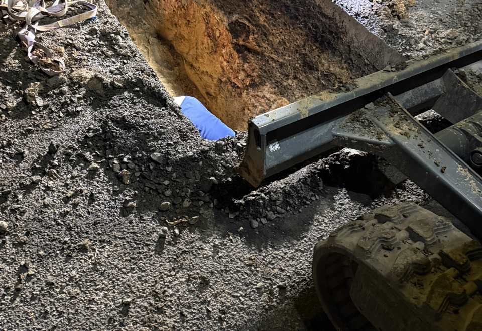 Minibagger arbeitet an einer tiefen rechteckigen Baugrube in einer befestigten Fläche