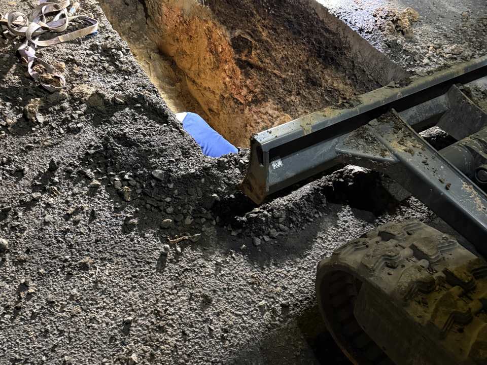 Minibagger arbeitet an einer tiefen rechteckigen Baugrube in einer befestigten Fläche