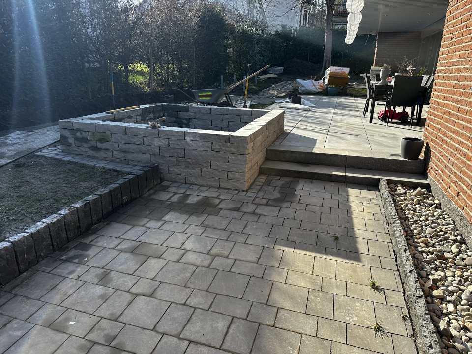 Gepflasterte Außenfläche mit Naturstein-Hochbeet, Stufenanlage und großformatiger Terrasse am Wohnhaus