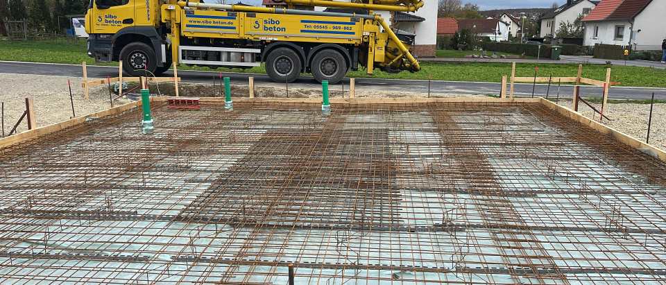 Großflächig bewehrte Bodenplatte mit mehreren grünen Rohrdurchführungen und Betonpumpe im Hintergrund