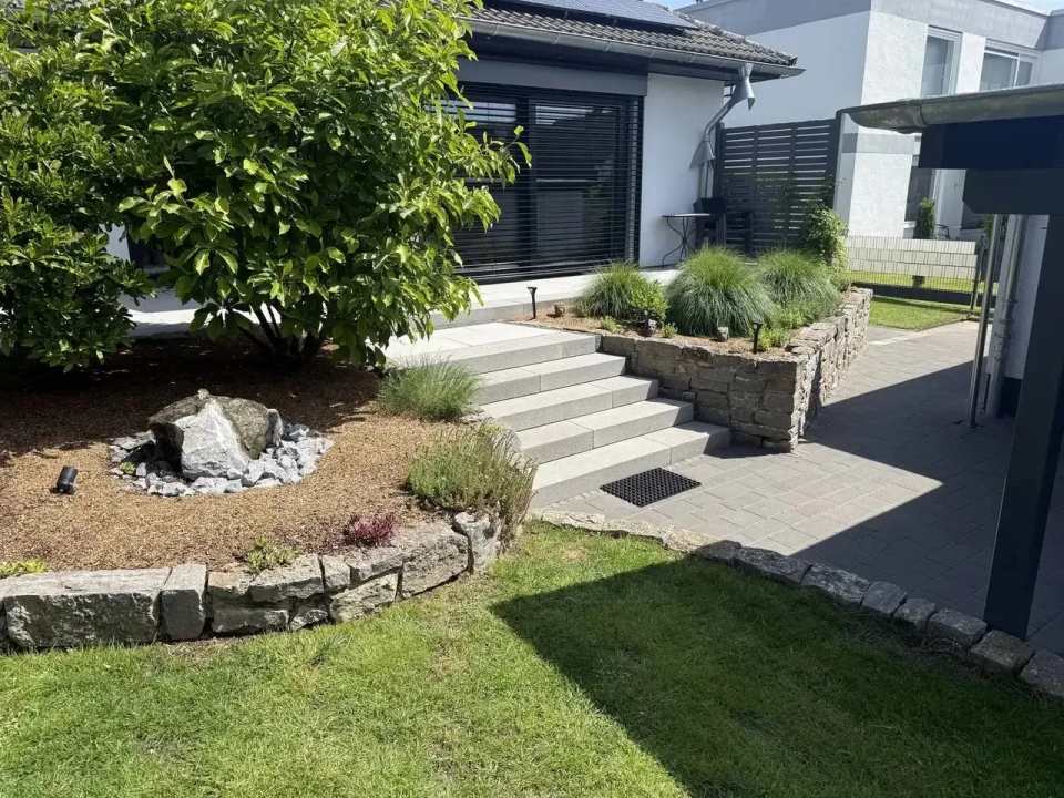 Gepflegte Gartenanlage mit Natursteinbeeten, breiter heller Treppenanlage und gepflastertem Zugang