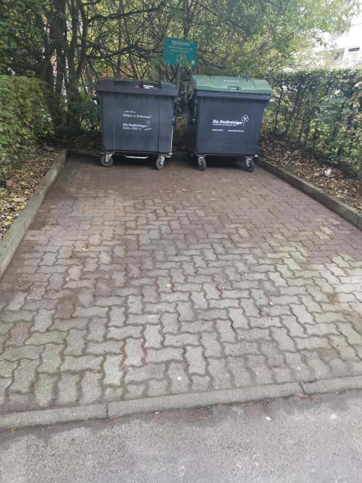 Gepflasterte Stellfläche mit zwei großen Abfallcontainern zwischen Hecken und Grünflächen