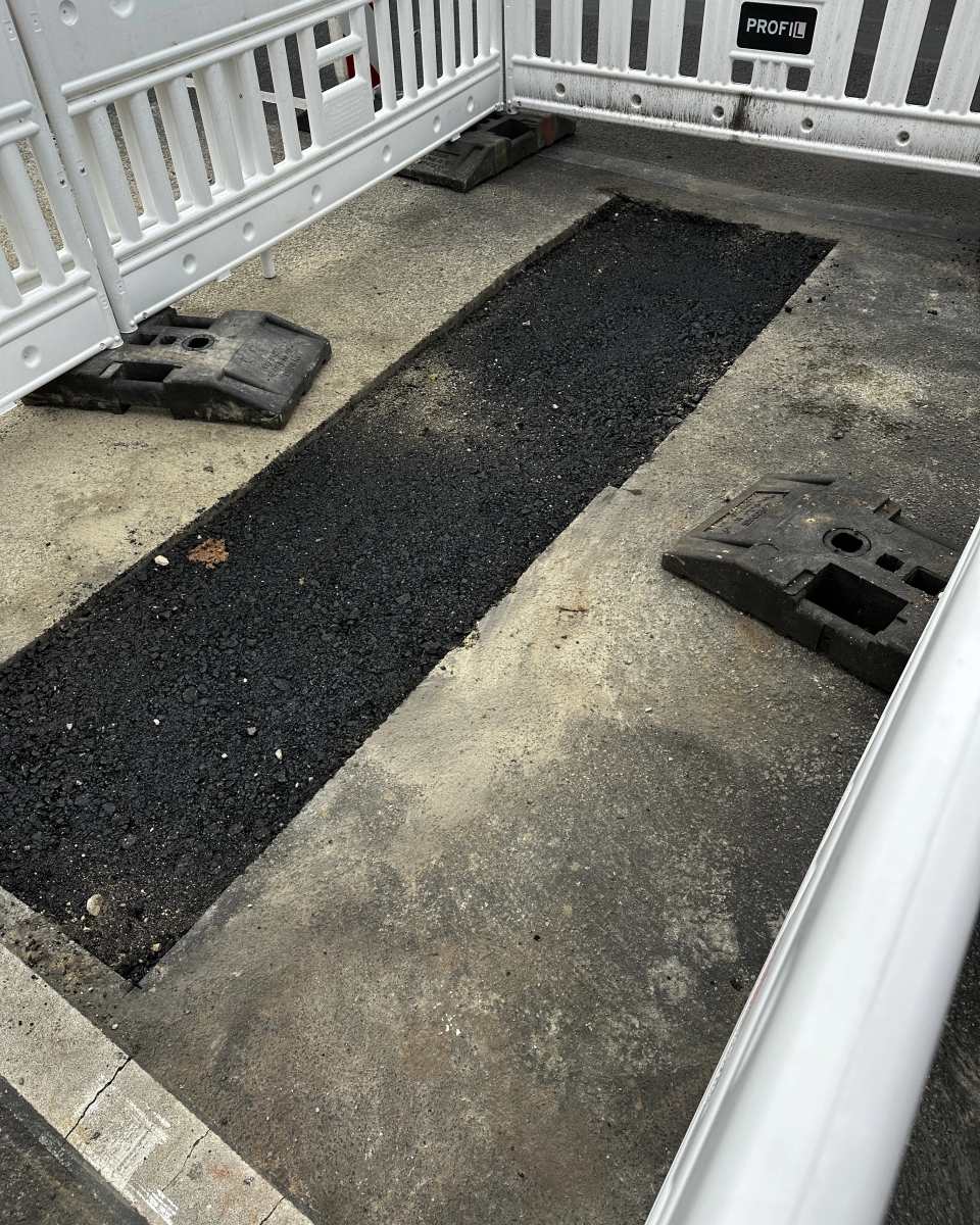 Frisch mit Asphalt verschlossene rechteckige Bauöffnung innerhalb einer abgesperrten Verkehrsfläche