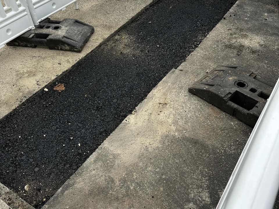 Frisch mit Asphalt verschlossene rechteckige Bauöffnung innerhalb einer abgesperrten Verkehrsfläche