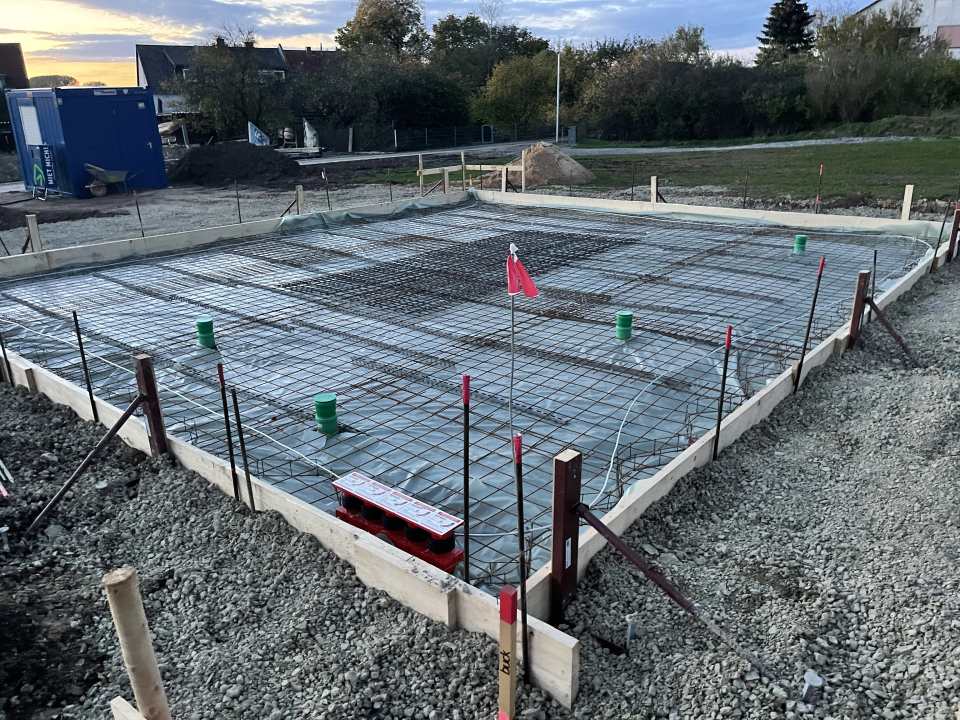 Große Bodenplatte mit flächiger Stahlbewehrung, Rohrdurchführungen und umlaufender Schalung auf einer Baustelle