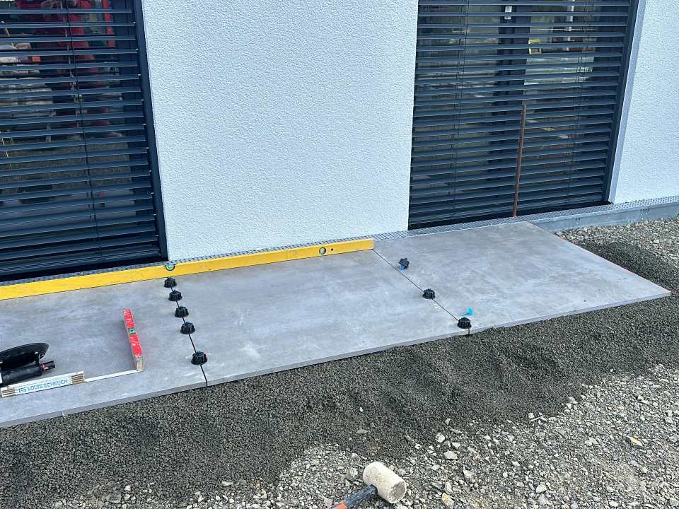 Großformatige graue Terrassenplatten auf verstellbaren Stelzlagern vor einer modernen Hausfassade