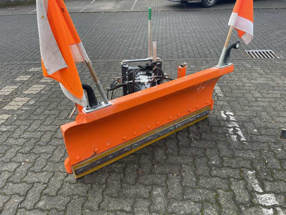 Orangefarbenes hydraulisches Schneeschild mit Warnflaggen auf einer gepflasterten Hoffläche