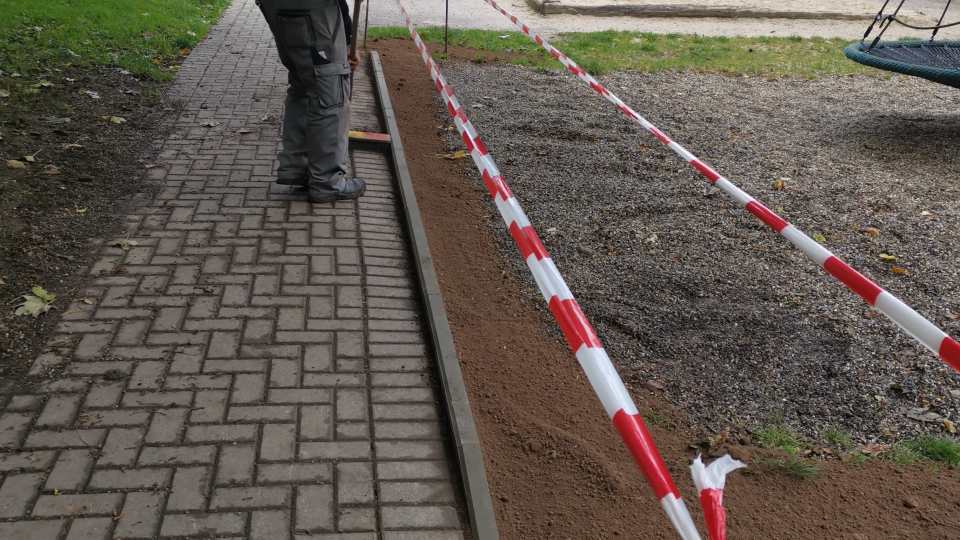 Mitarbeiter richtet eine lange Randeinfassung entlang eines gepflasterten Gehwegs in einem abgesperrten Außenbereich aus