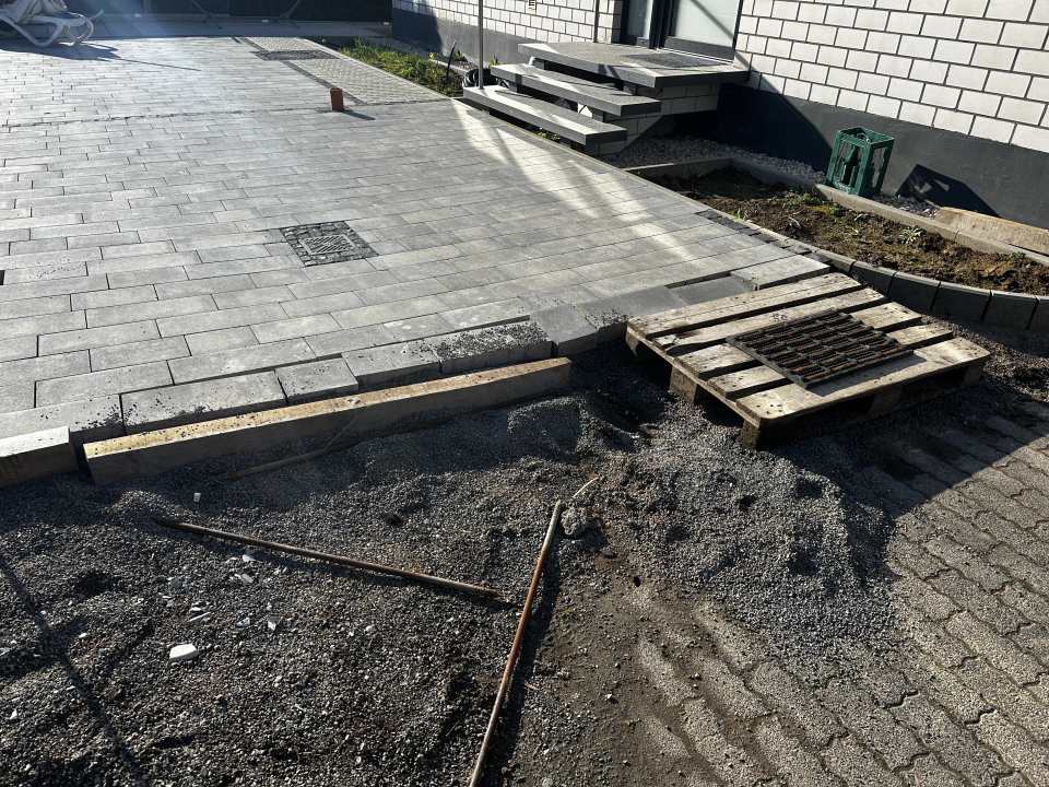 Großflächige graue Pflasterfläche vor einem Gebäude mit Stufenanlage und noch offenem Anschlussbereich